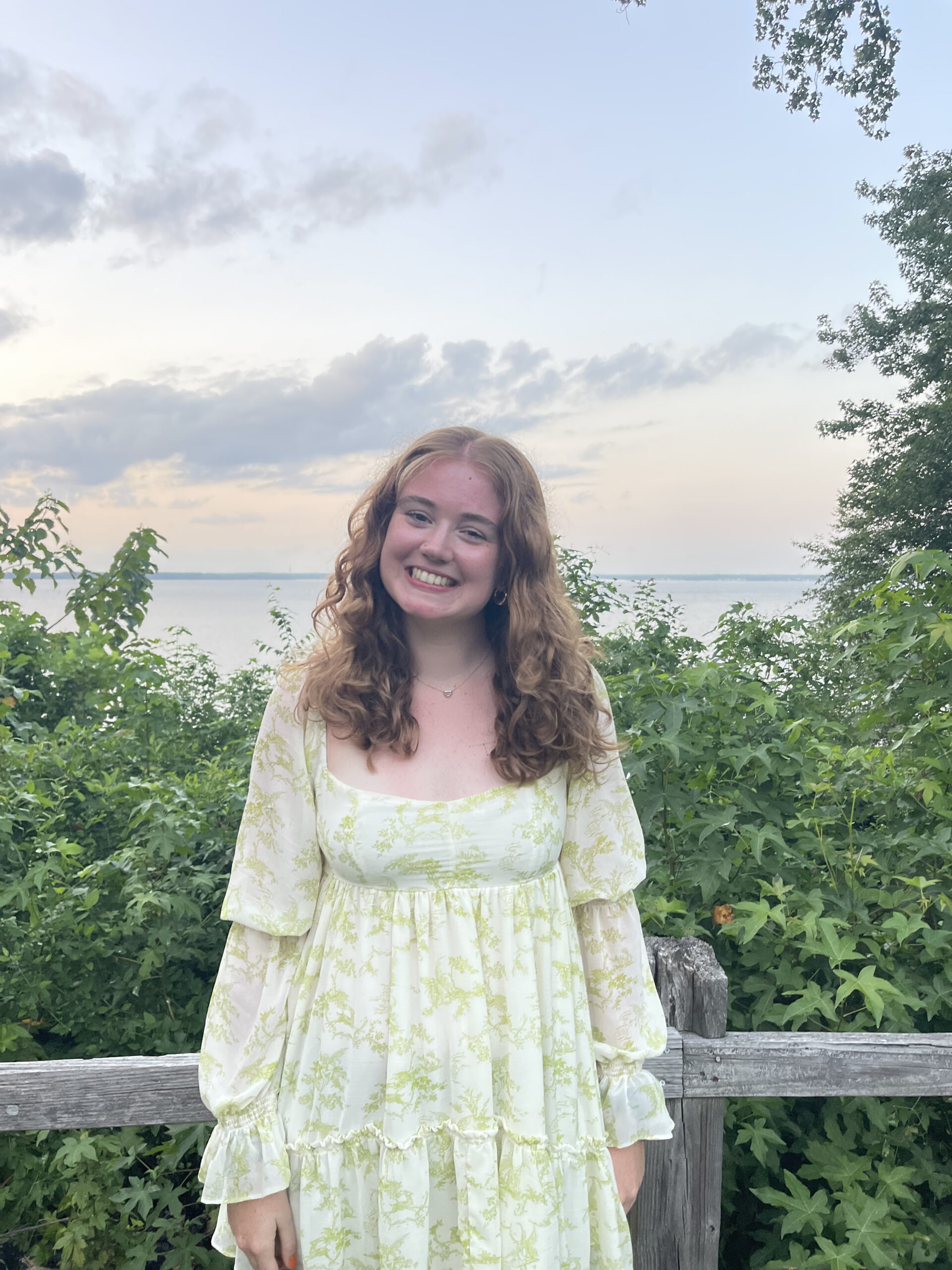 Hannah Holstrom standing outside in front of a fence with a sunset behind her